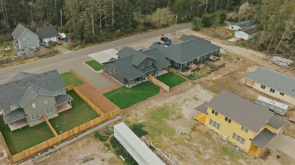 Aerial view over a new development: a dark-sided duplex, fenced lawns, and homes under construction