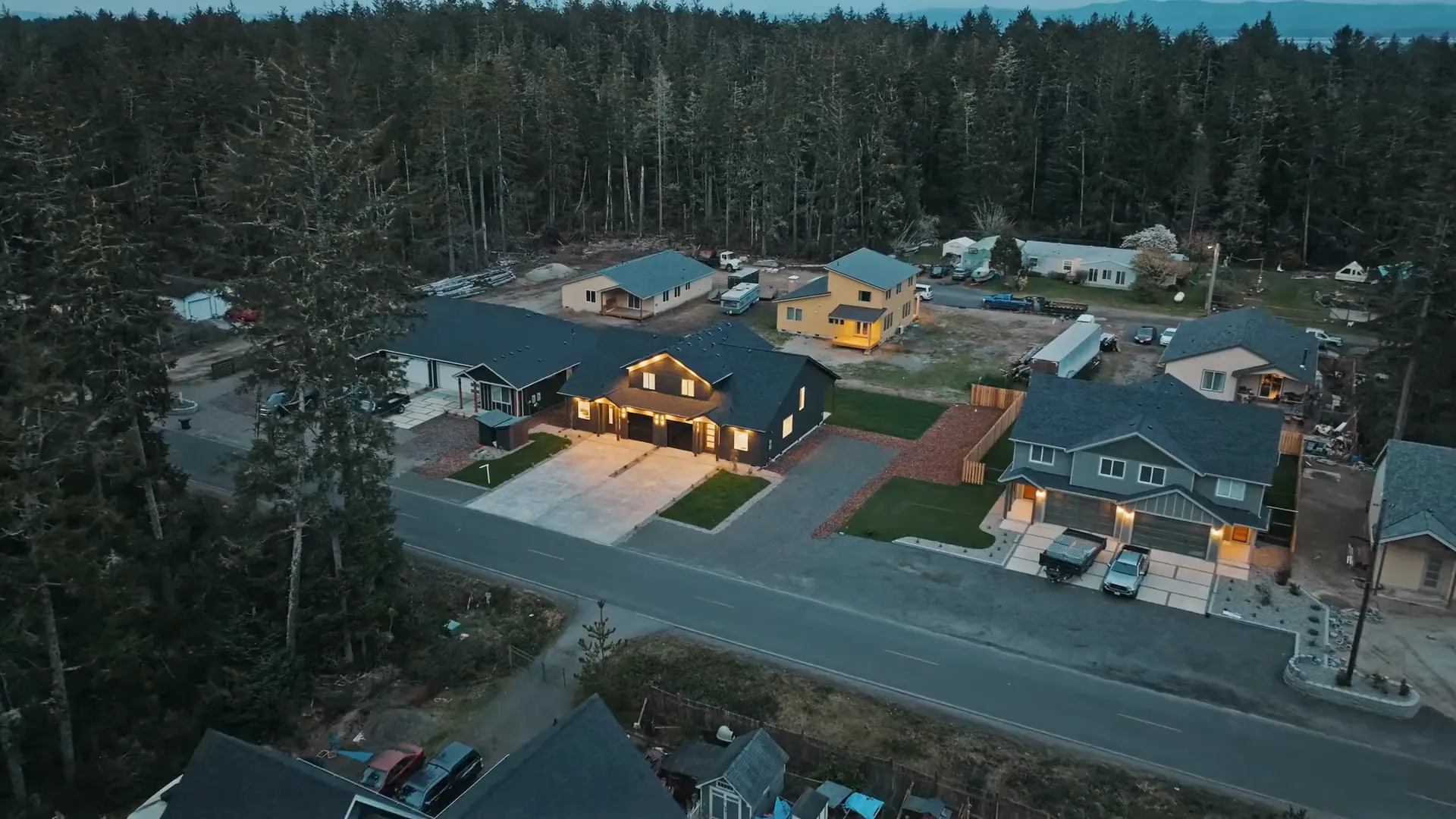 Twilight aerial of a new-build duplex with its lights on, among the trees of a new development