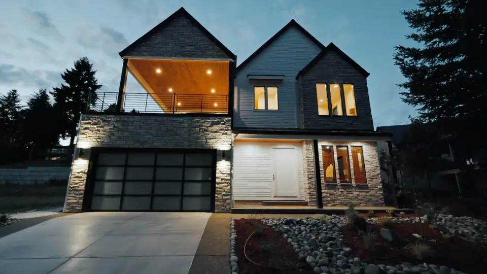 A modern two-story home with stone and dark siding, lit at dusk